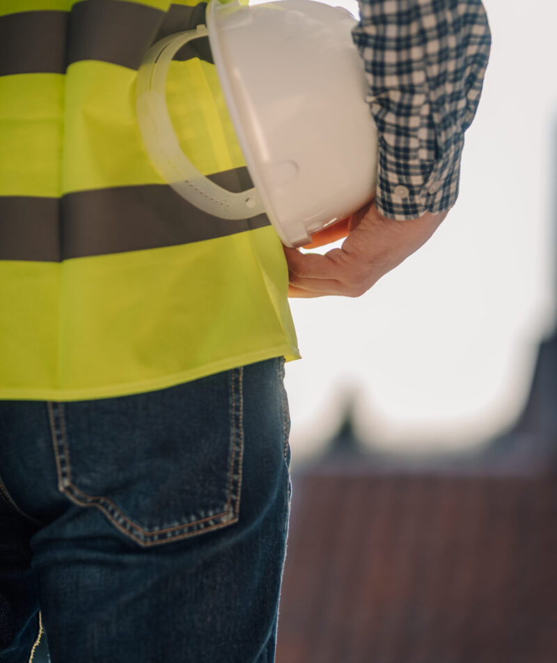 Construction worker wearing high-visibility vest holding white hardhat at construction site